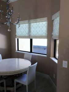 3 White Classic Roman Shades with Embroidery in a Lattice Like Pattern in a Dining Area